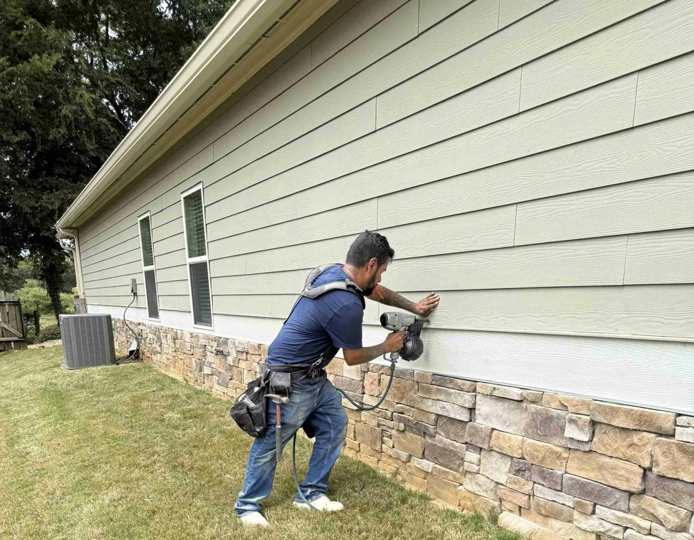 Technician nailing new fiber cement lap siding onto a home